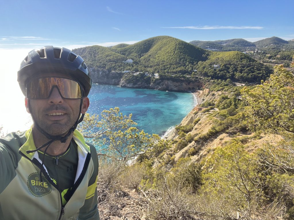 Cyclist taking a selfie above a turquoise bay on the Ibiza coast